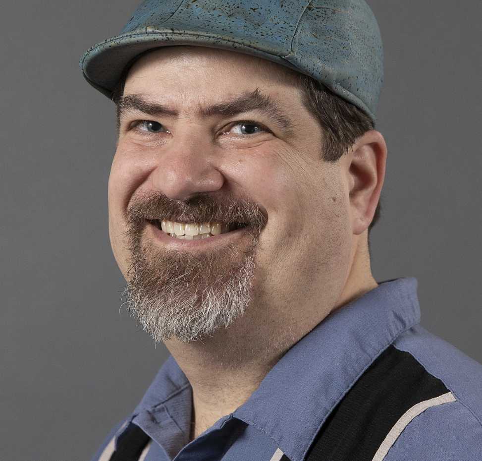 A portrait of José Perillán, a person in a blue shirt and derby hat.
