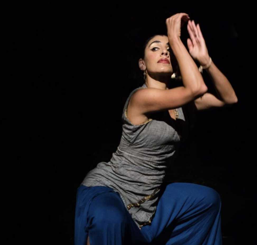 A person in a dancing pose on on a darkened stage.